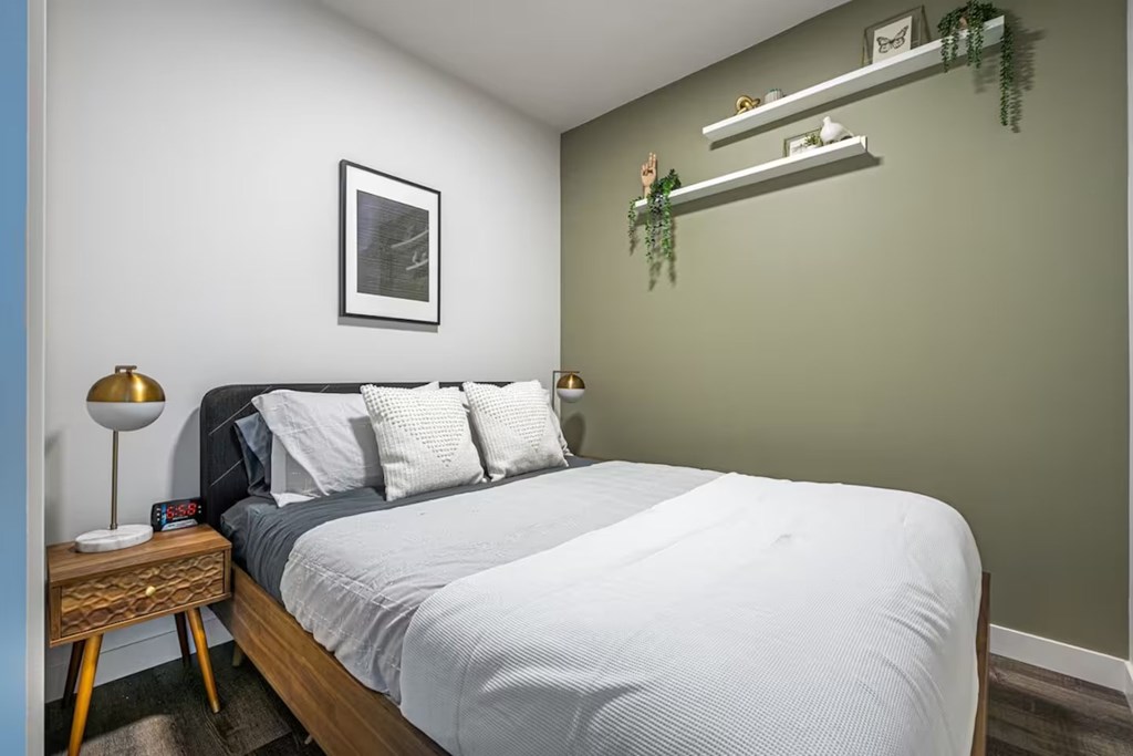 A bedroom with a bed, nightstand, and a picture on the wall.