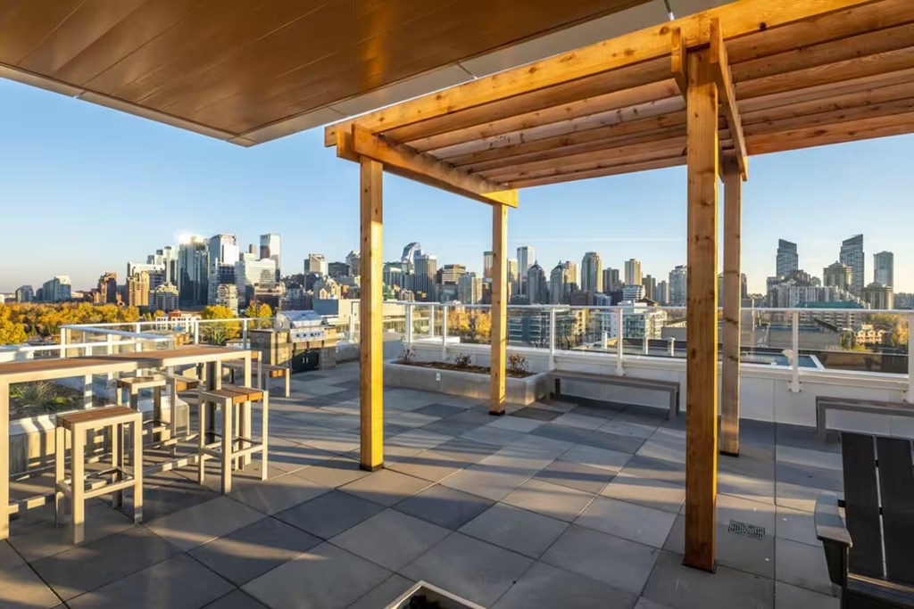 A wooden pergola is over a table and chairs on a rooftop.