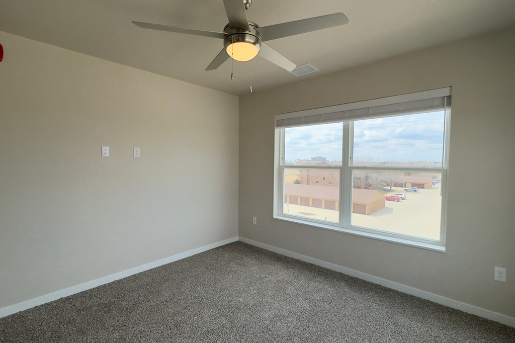 Empty room with a ceiling fan and a window overlooking a parking lot.