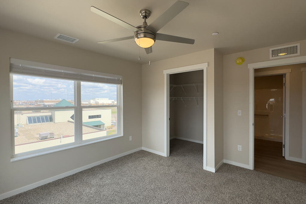 A room with a ceiling fan and a large window overlooking a parking lot.
