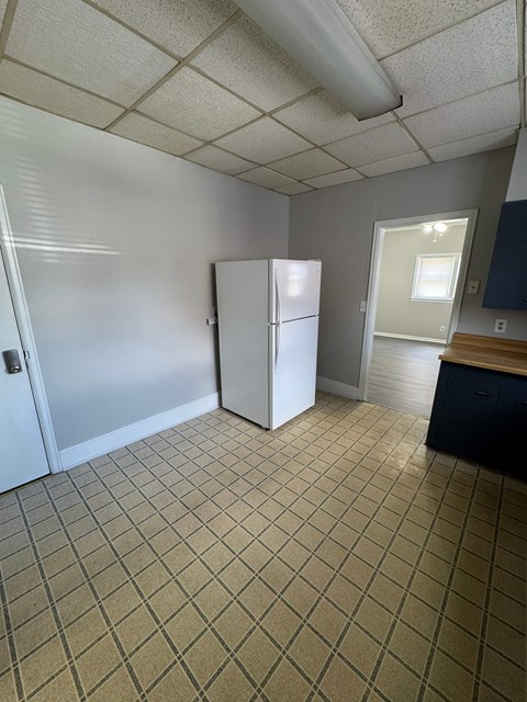 A kitchen with a white fridge and a tiled floor.