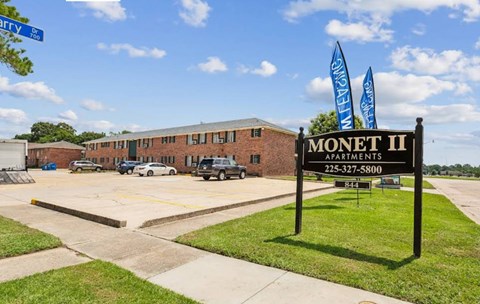 A sign for Monet II Apartments stands in front of a parking lot.
