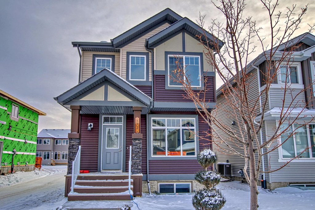 A house with a grey front and a brown roof with a snow covered ground.