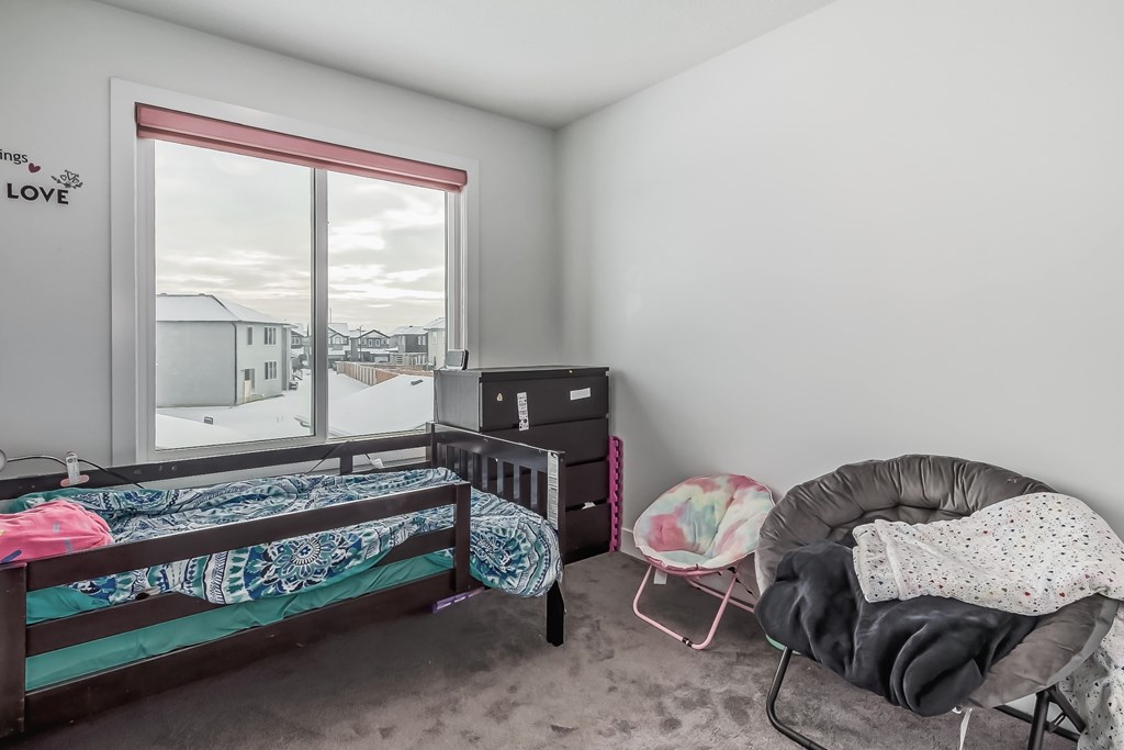 A bedroom with a bed, chair, and a window with a view of houses outside.