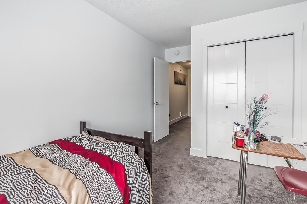 A bedroom with a bed, a chair, and a table with a vase of flowers on it.