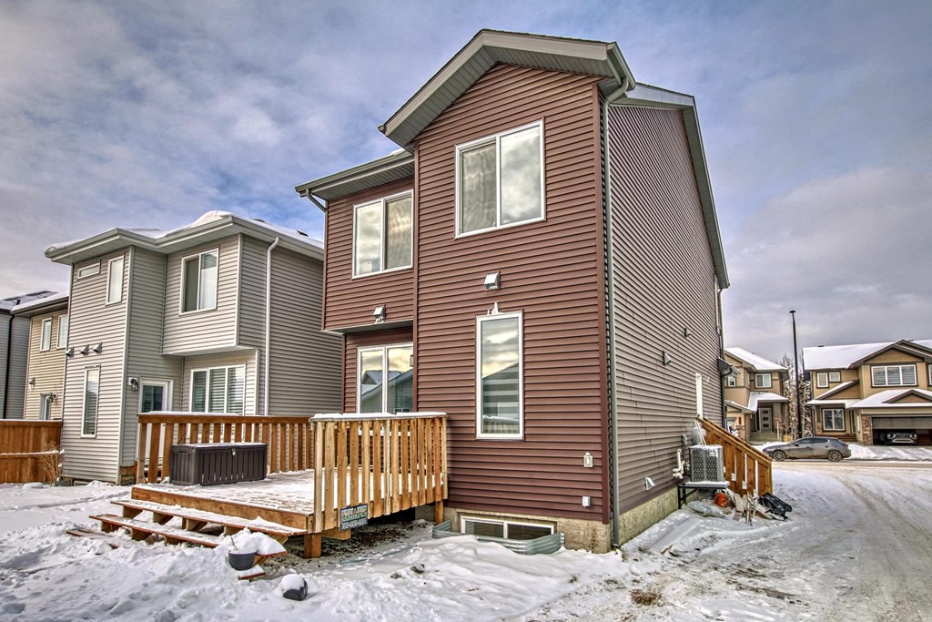 A house with a brown siding and a wooden deck in the snow.