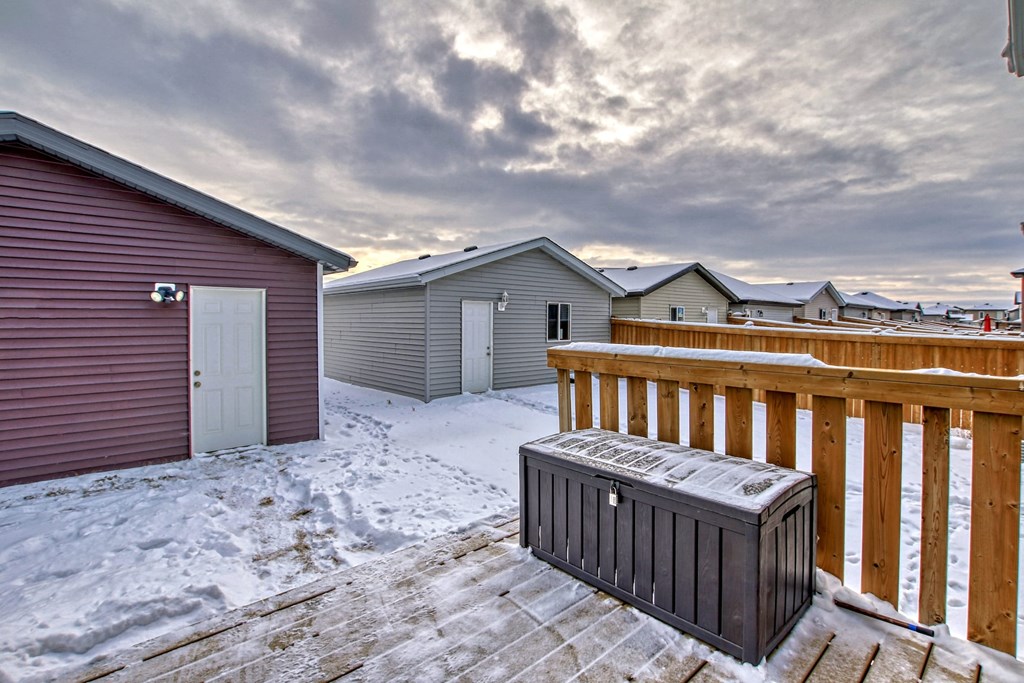 A black cooler is on a wooden deck in front of a red building.