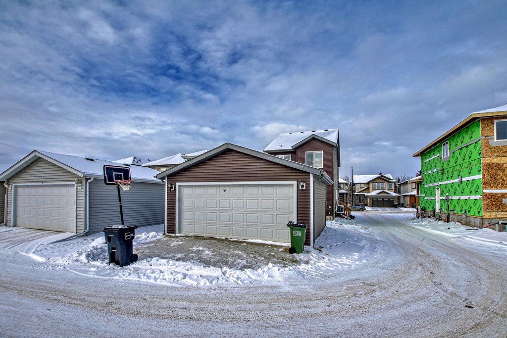 A snowy residential street with a green trash can and a basketball hoop.