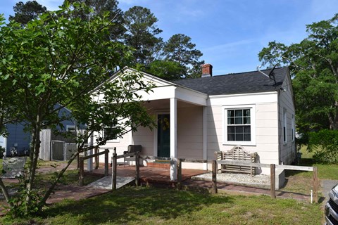 A small white house with a porch and a tree in front.