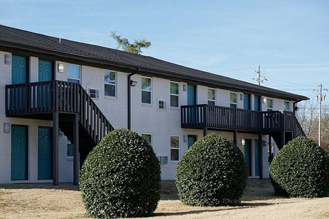 A building with a balcony and two bushes in front.