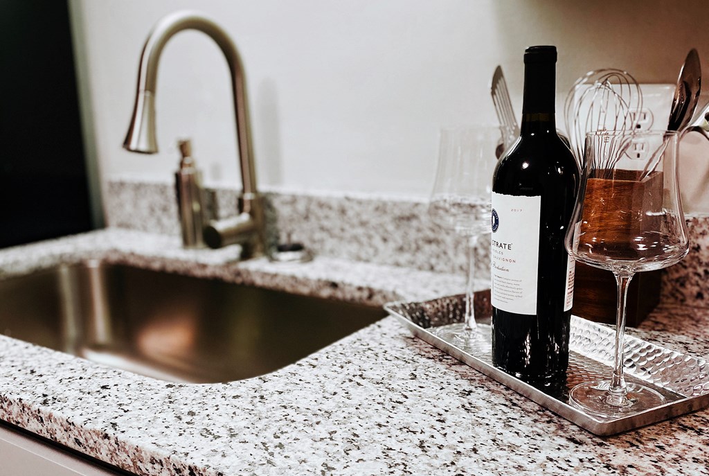 A bottle of wine is placed on a tray next to a wine glass on a kitchen counter.