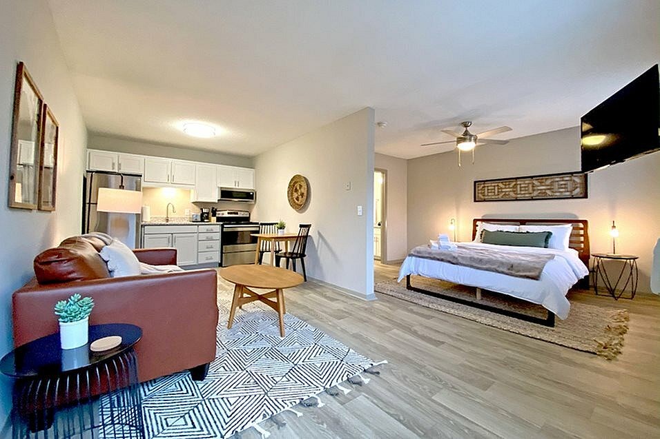 A living room with a red couch and a bedroom with a bed and a dresser.