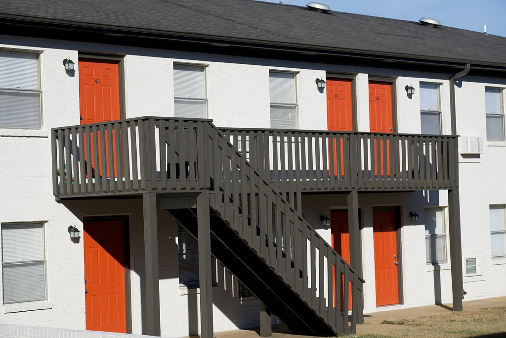A white building with a black roof and a balcony with orange doors.