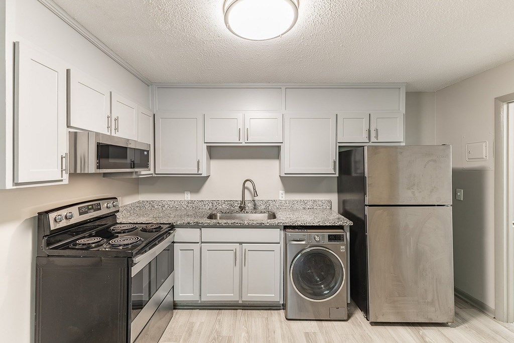 A kitchen with a black stove top oven, a granite counter top, and a washer and dryer.