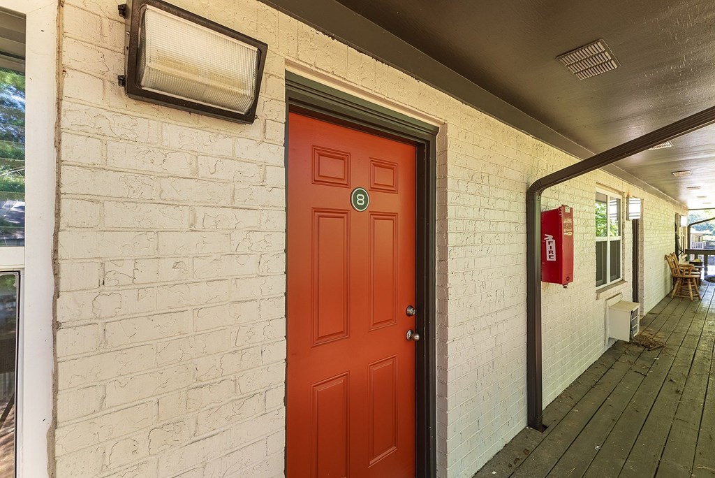 A red door is on the left side of a white brick wall.