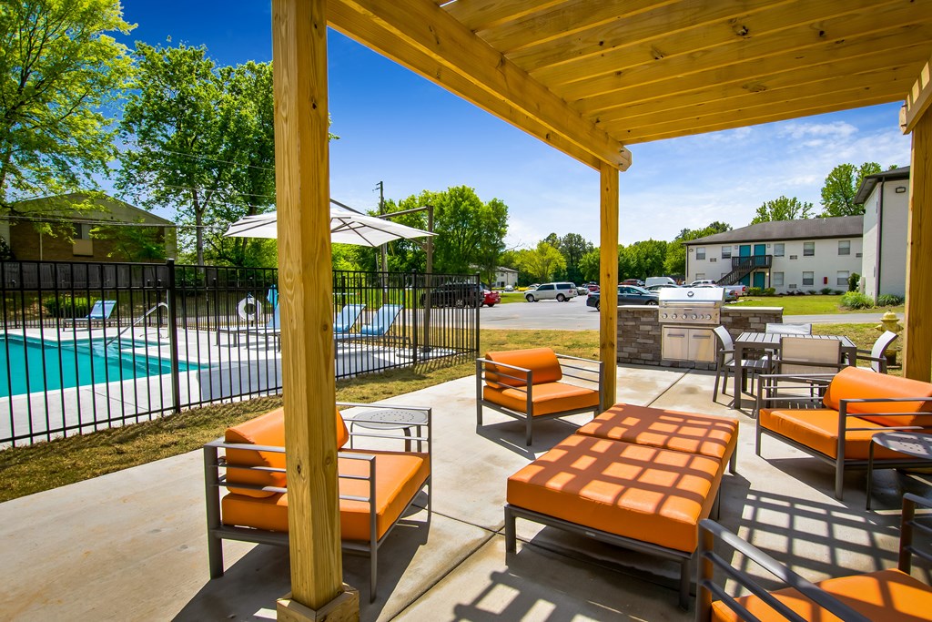 A wooden patio with orange cushions and a pool in the background.