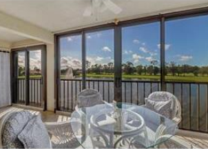 A glass table with chairs is in front of a balcony with a view of the outdoors.