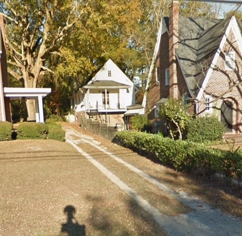 A white house with a black roof is surrounded by trees and bushes.