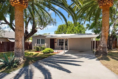 A house with a driveway and palm trees in front.
