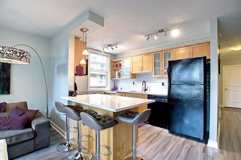 A kitchen with a black refrigerator and a bar area with stools.