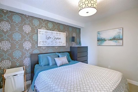 A bedroom with a bed, a pillow, a nightstand, a lamp, a painting, and a sign on the wall.