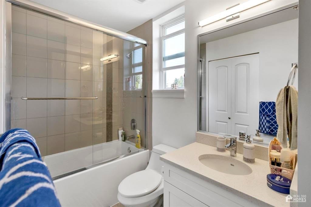 A white bathroom with a white toilet, sink, and a glass shower stall.