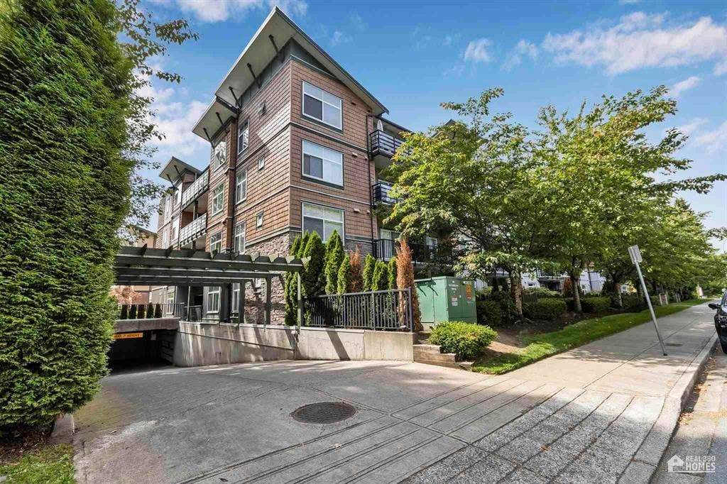 A modern apartment building with a green fence and a tree in front.