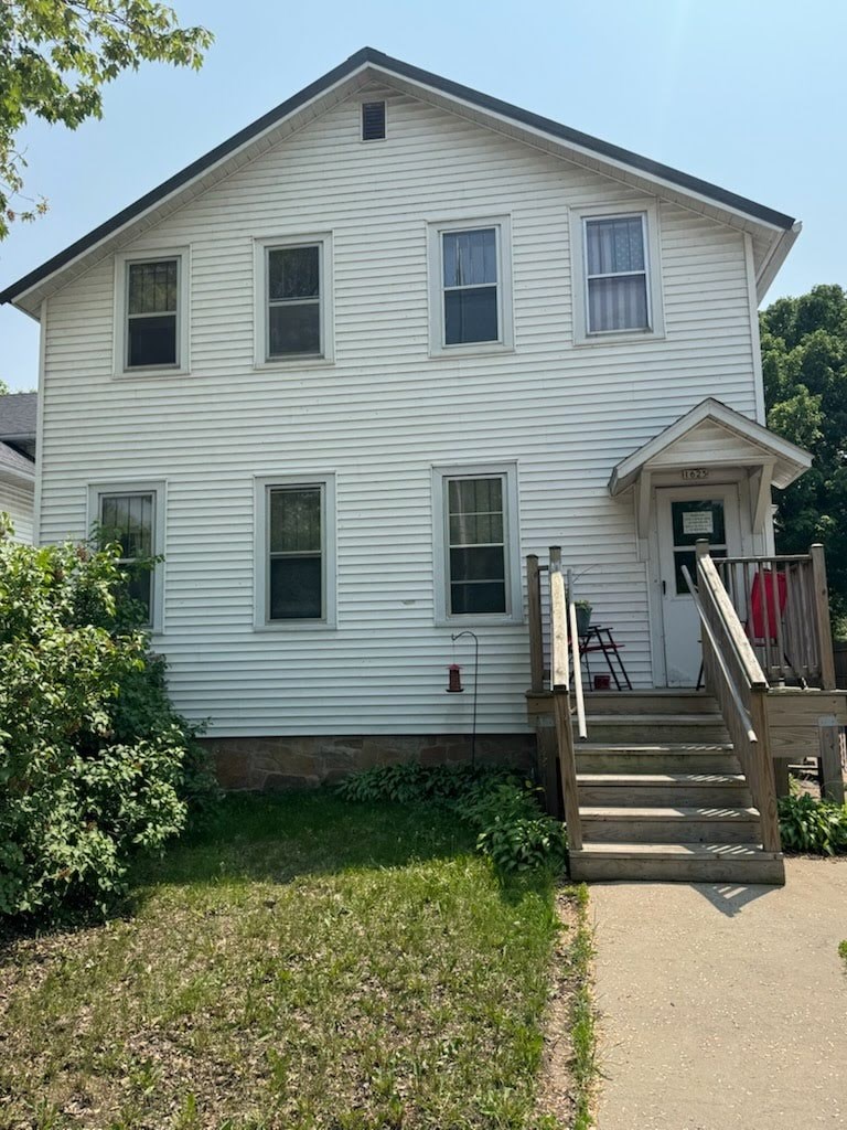 A white house with a grey roof and a wooden staircase leading to the front door.