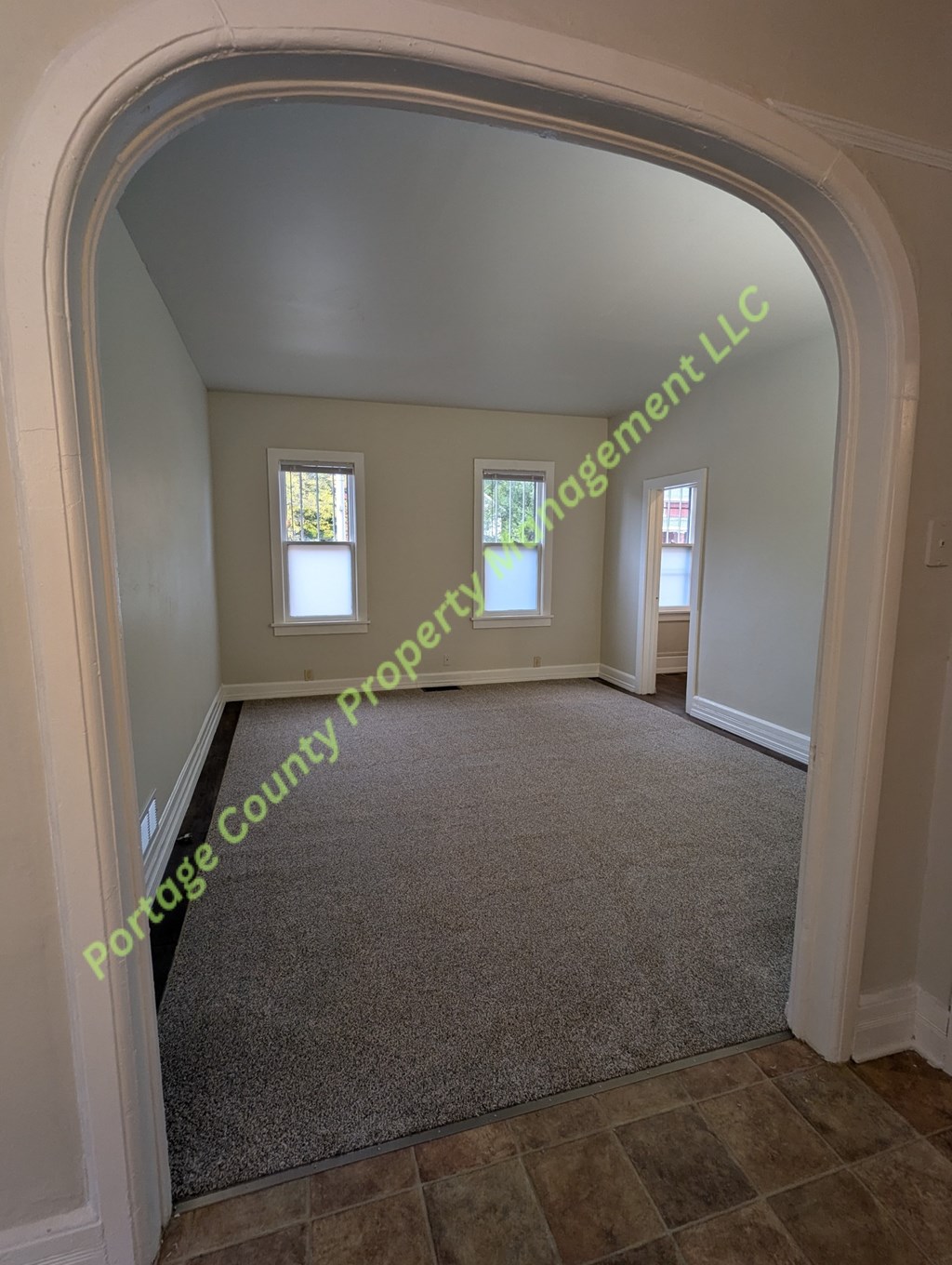 A carpeted room with a window and a doorway leading to another room.