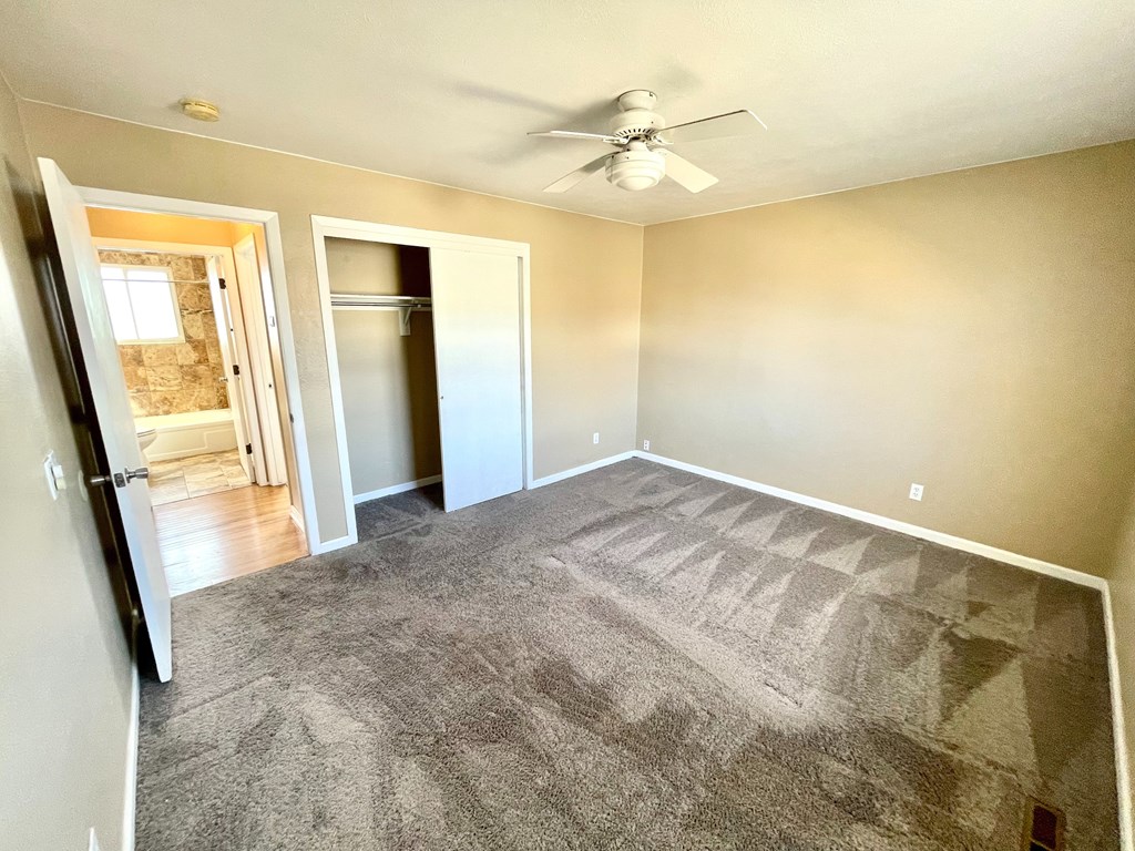A room with a grey carpet and a ceiling fan.