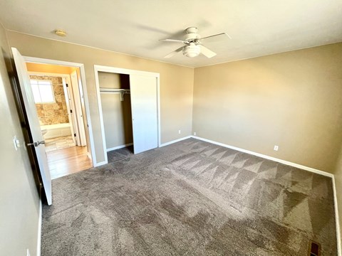 A room with a grey carpet and a ceiling fan.