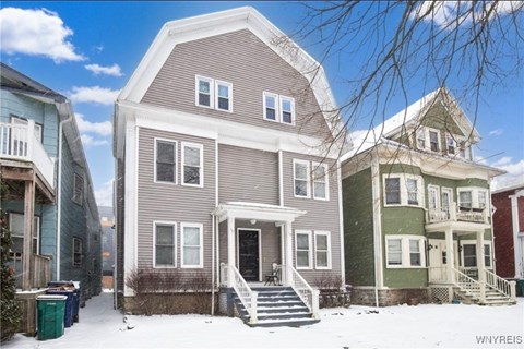 A house with a grey front and a white door is in the snow.