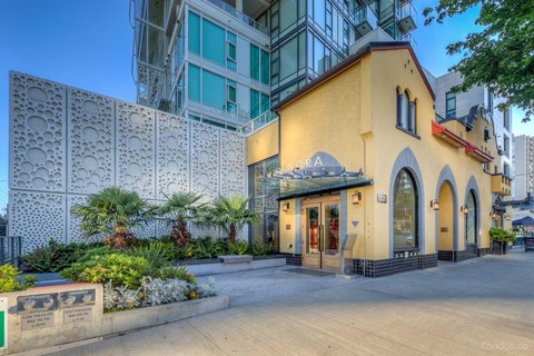 A building with a yellow facade and a sign that reads "CANDORA" is surrounded by a white lattice fence and greenery.