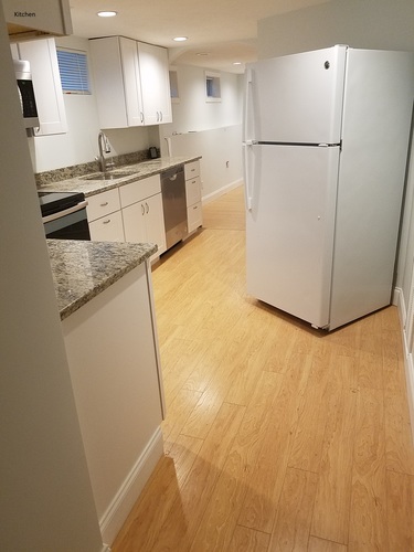 A white refrigerator stands in a kitchen with wooden floors.