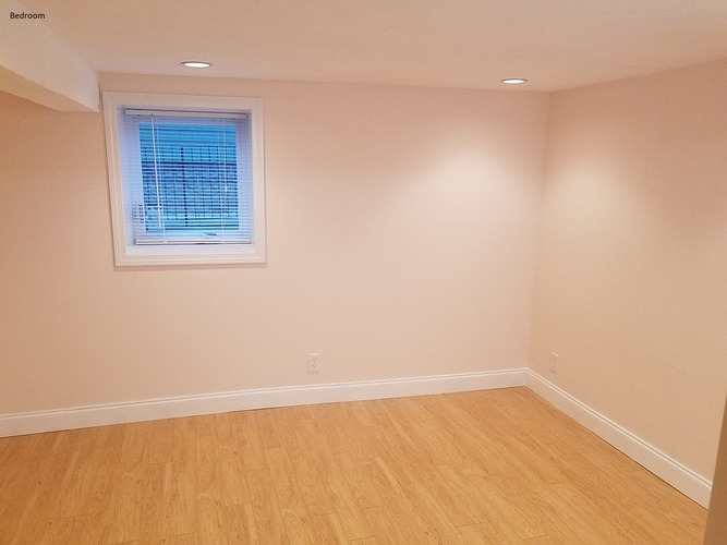 A bedroom with a window and wooden flooring.