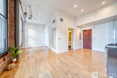 A spacious room with wooden floors and a brick wall on the left side.