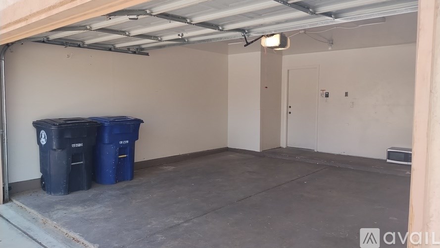 A storage room with a blue and black trash can under a metal roof.