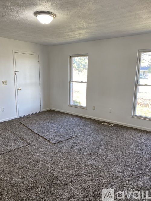 A room with a carpeted floor, a door, and two windows.