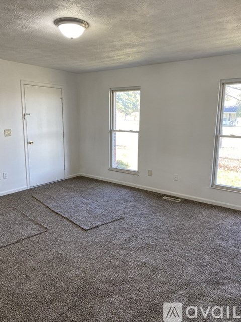 A room with a carpeted floor, a door, and two windows.