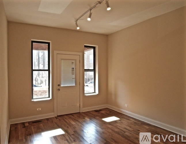 A room with wooden floors and two windows, one of which has a view of a street.