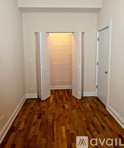 A room with wooden floors and white walls has a doorway leading to another room.