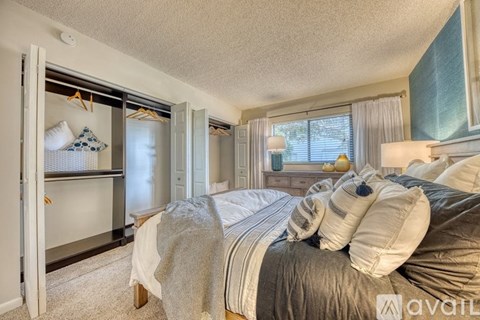 A bedroom with a bed, a window with curtains, and a closet with clothes hanging.