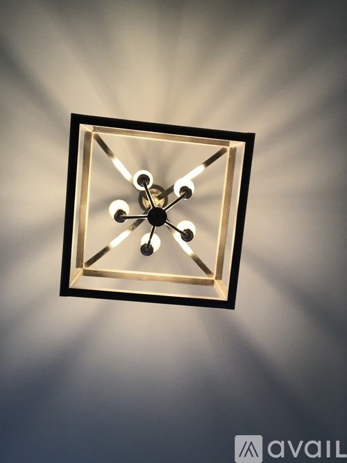 A square clock with a black frame and gold accents is mounted on a wall.
