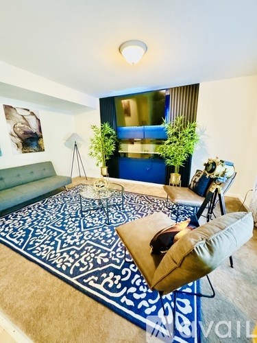 A living room with a blue and white patterned rug, a green sofa, and a small table with a lamp and a plant.
