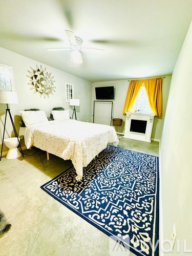 A bedroom with a bed, a rug, a ceiling fan, and a wall decoration.