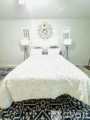 A bed with a white comforter and a black and white patterned rug in front of it.