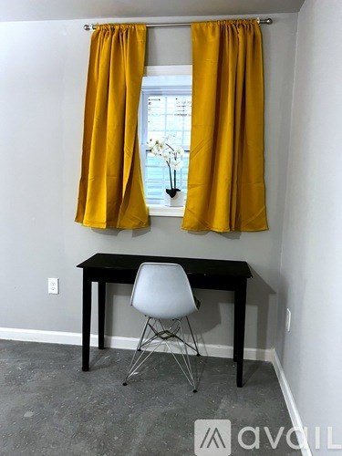 A table with a chair and a window with yellow curtains.