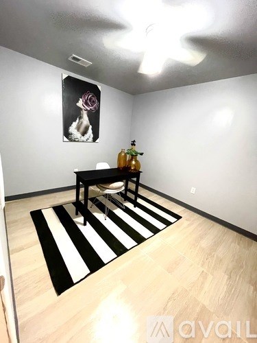 A black and white striped rug sits on a wooden floor in a room with a white wall and a picture of a woman with a pink flower in her hair.