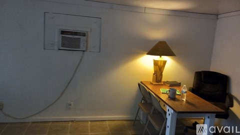 A lamp on a desk in a room with a white wall and a window vent.