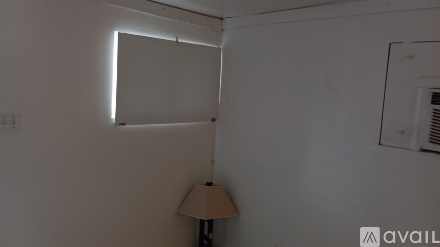 A lamp sits on a table in a room with a white wall and a window.